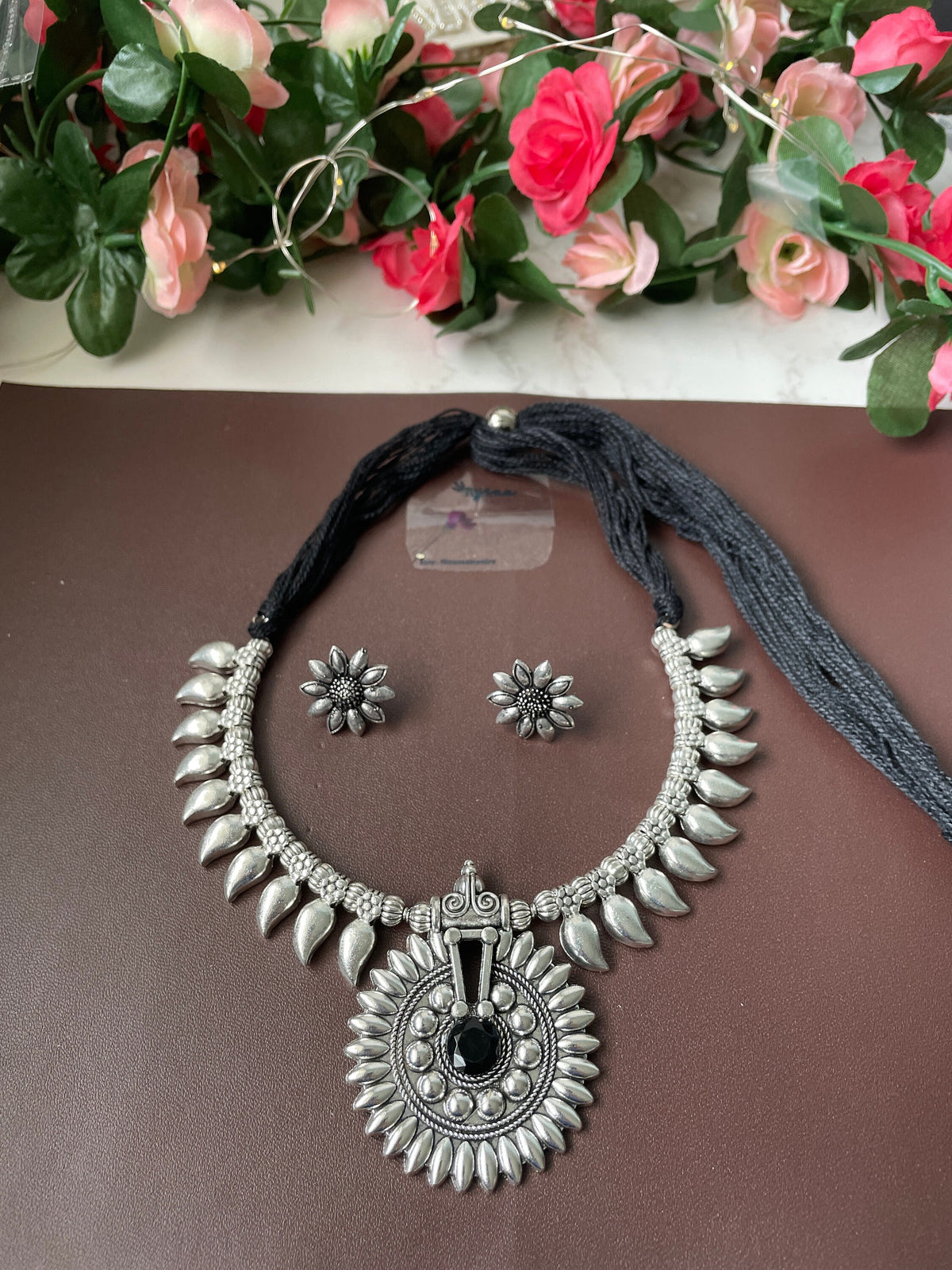 A silver necklace with a black stone pendant and matching earrings. The necklace features a large, ornate pendant with a black stone in the center. The earrings are small and simple, with a single black stone each.