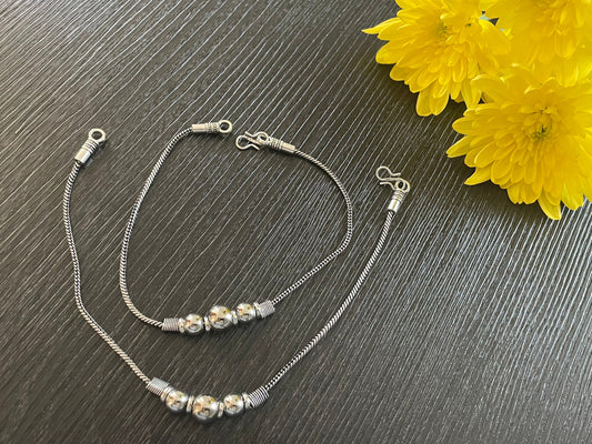 silver anklets with a chain design and a row of silver beads. The anklets are on a dark gray surface.