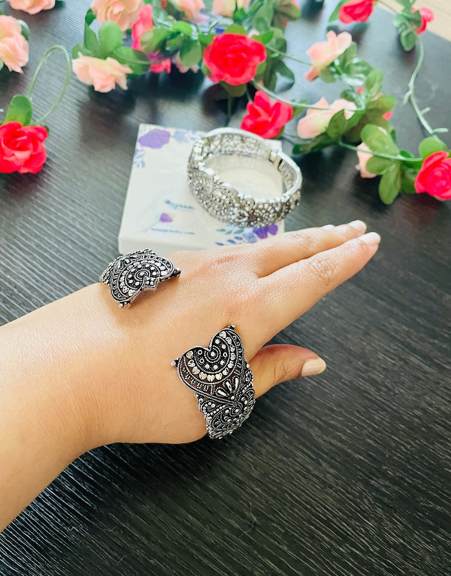 Silver-toned jewelry set featuring a heart-shaped cuff bracelet, a matching ring, and a hinged bracelet. The pieces are adorned with intricate filigree. A small box is visible in the background.