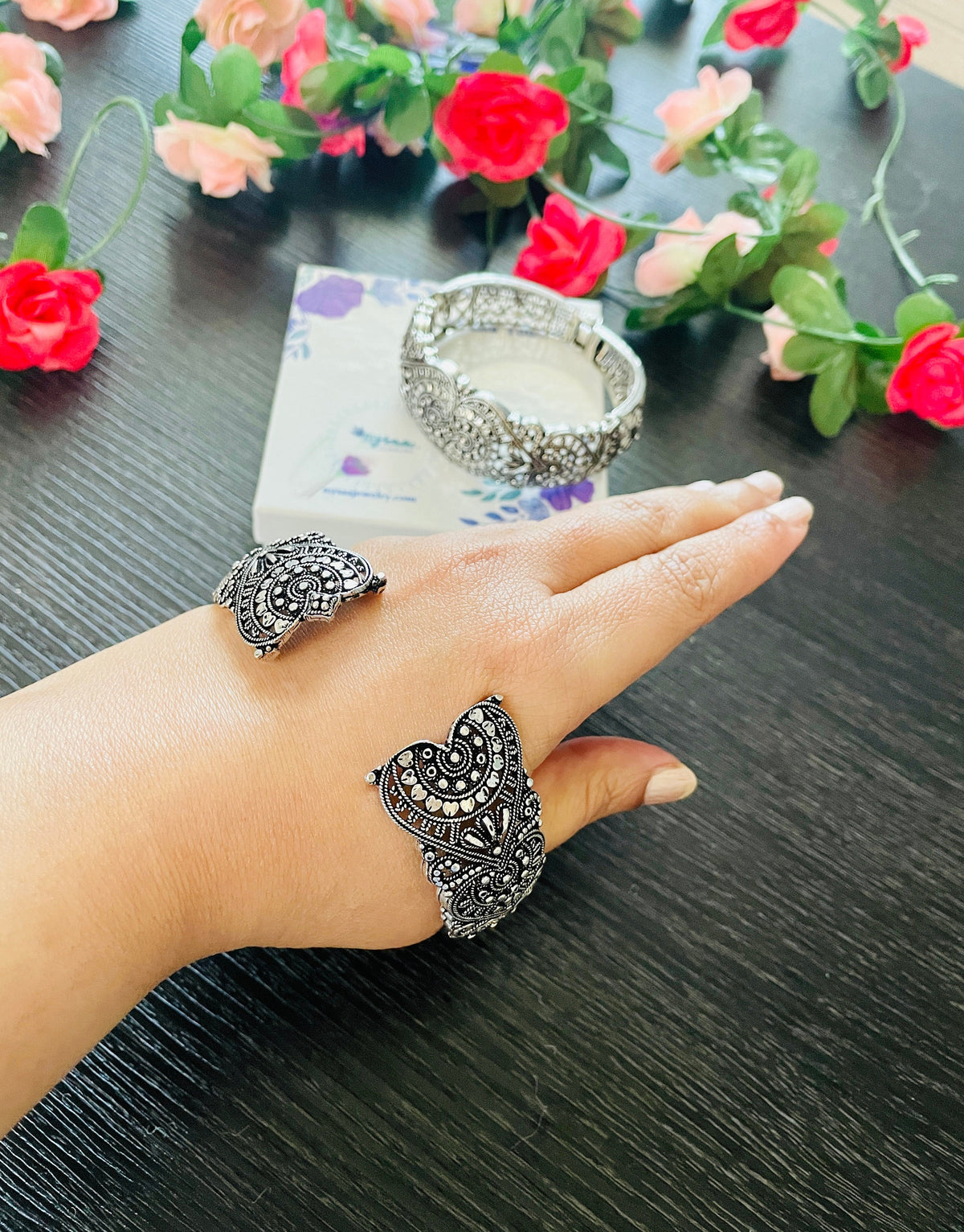 Silver-toned jewelry set featuring a heart-shaped cuff bracelet, a matching ring, and a hinged bracelet. The pieces are adorned with intricate filigree. A small box is visible in the background.