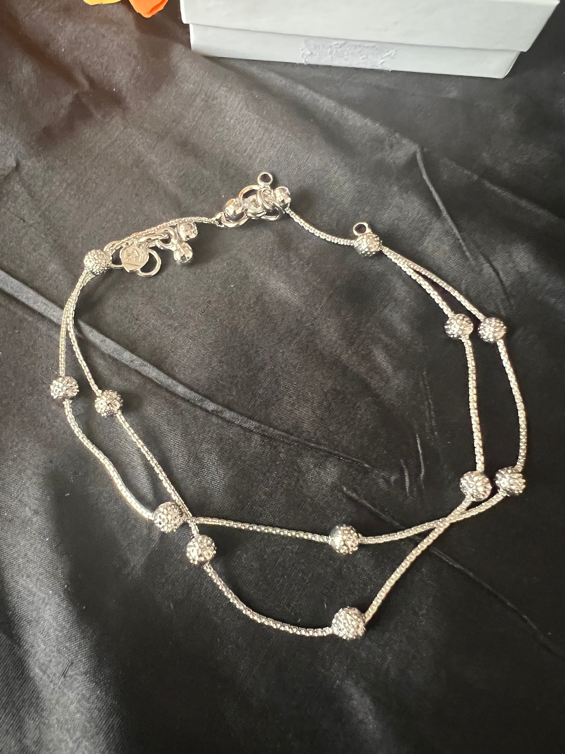 A silver anklet with two rows of small, round, textured beads. The anklet has a silver clasp and a silver chain.