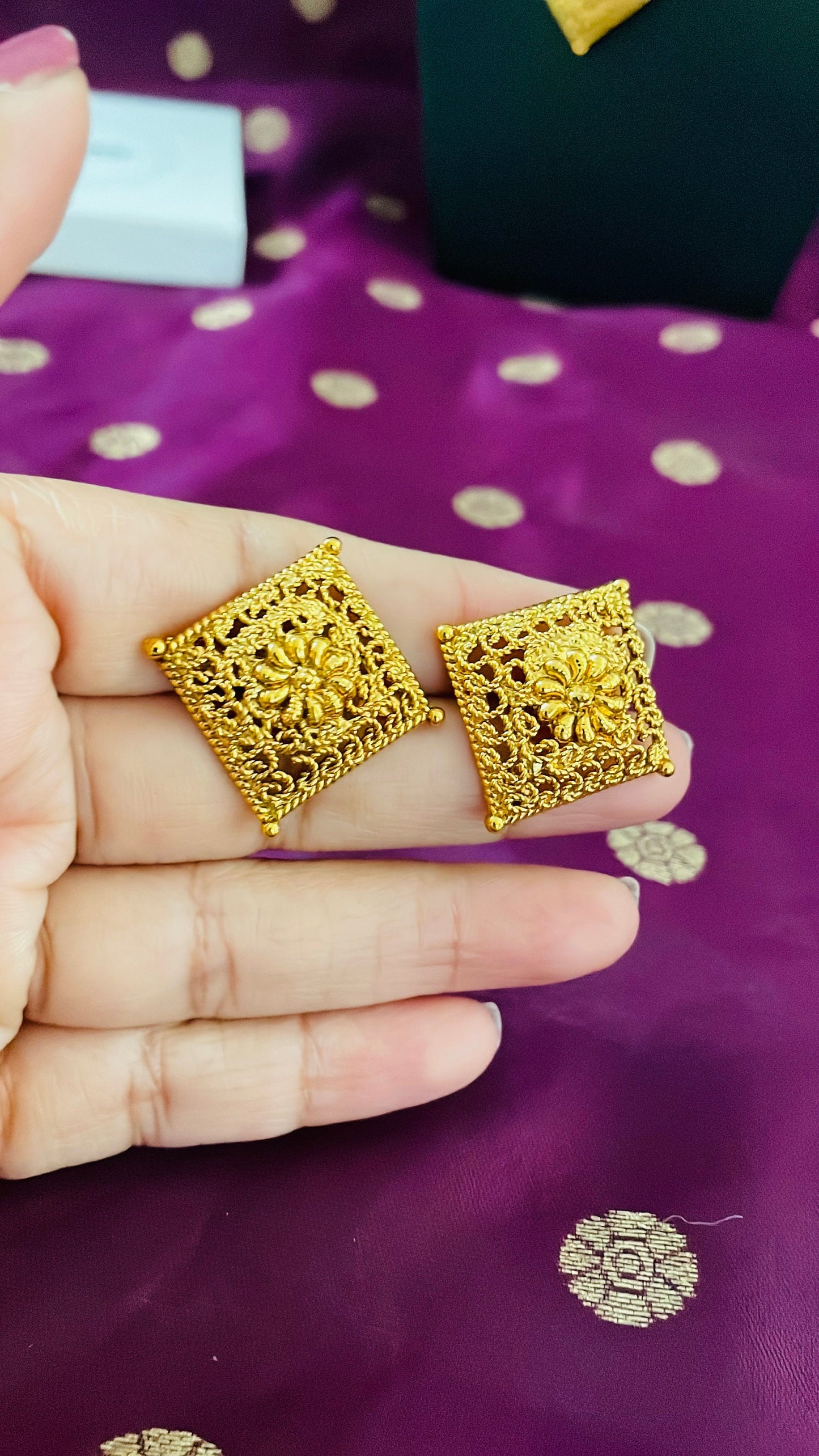 Two gold square earrings with intricate floral designs. The earrings are made of a delicate, filigree-like metal and have a shiny, polished finish.
