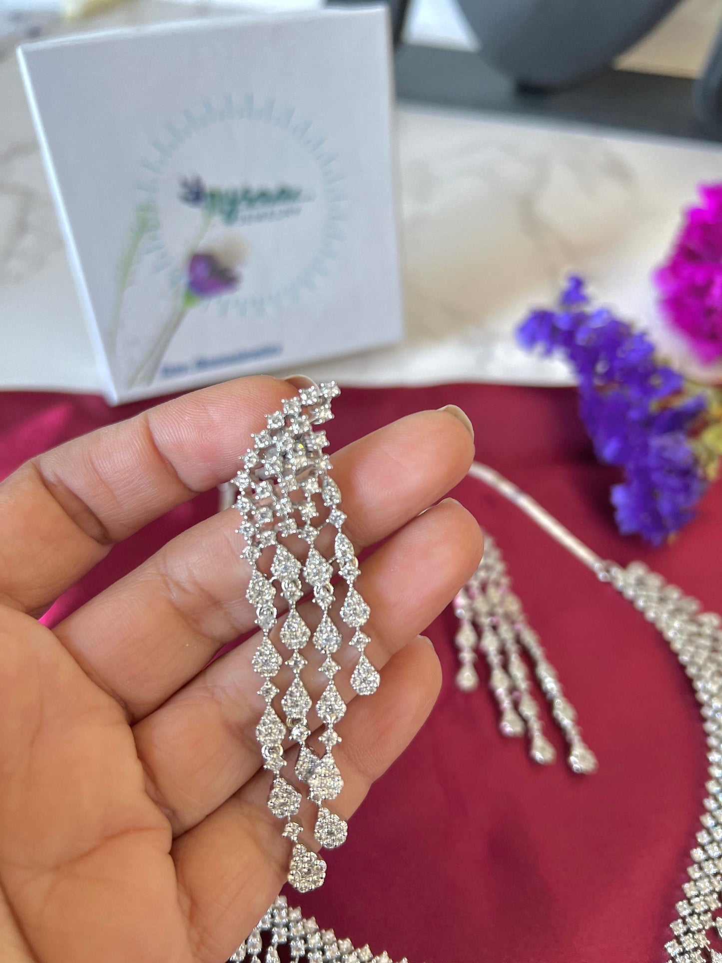 A silver necklace and earrings set with teardrop shaped crystal accents. The necklace and earrings are made of small, clear crystals that are arranged in a cascading pattern.