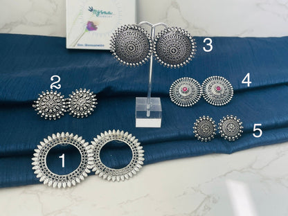 Different designs of stud Oxidised earrings. The earrings are numbered 1 through 5. Earrings 1 are large and round with a circle in the center. Earrings 2 are round with a floral design. Earrings 3 are round with a mandala design. Earrings 4 are round with a floral design and a pink stone in the center. Earrings 5 are round with a floral design.