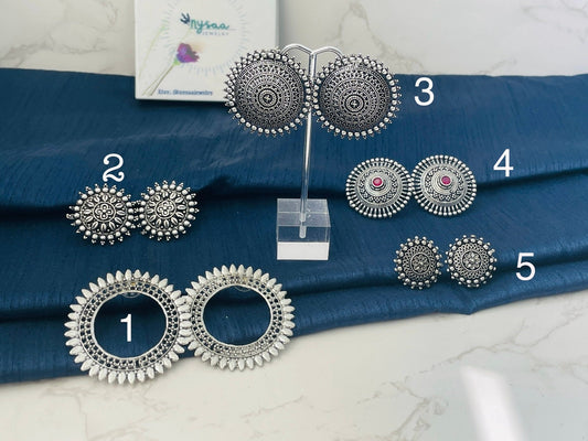Different designs of stud Oxidised earrings. The earrings are numbered 1 through 5. Earrings 1 are large and round with a circle in the center. Earrings 2 are round with a floral design. Earrings 3 are round with a mandala design. Earrings 4 are round with a floral design and a pink stone in the center. Earrings 5 are round with a floral design.