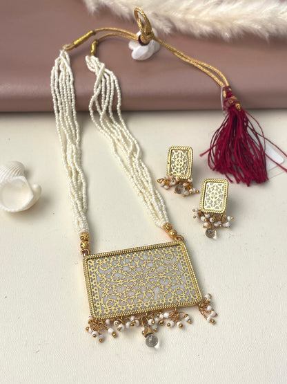 A gold and white thewa necklace and earrings set. The necklace has a rectangular pendant with a white center and intricate gold filigree design. The pendant is attached to a string of white beads. The earrings are also rectangular with a white center and gold filigree design. The earrings are attached to a string of white beads.