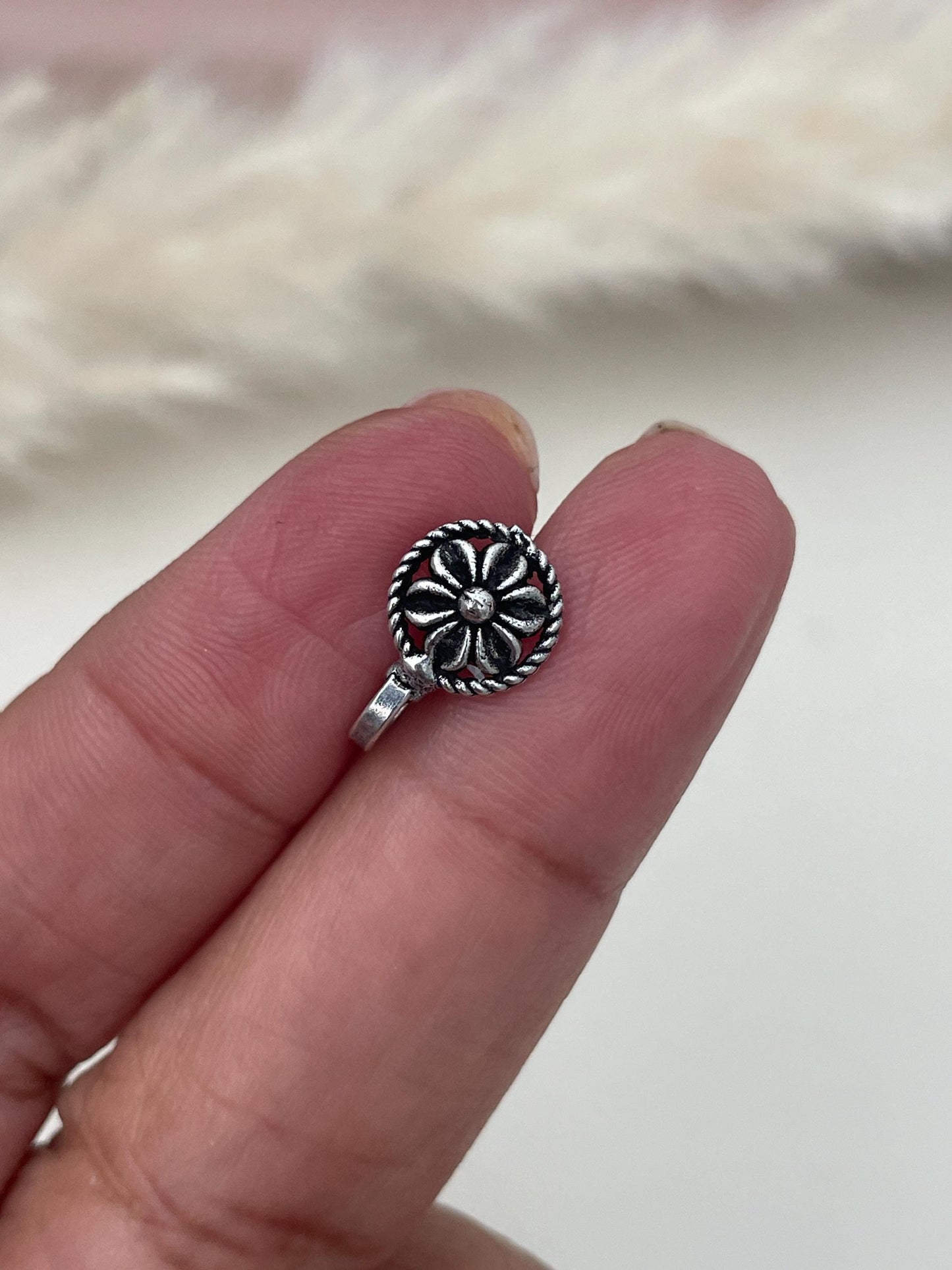 A silver lookalike nose pin with a flower design. Easy on nose