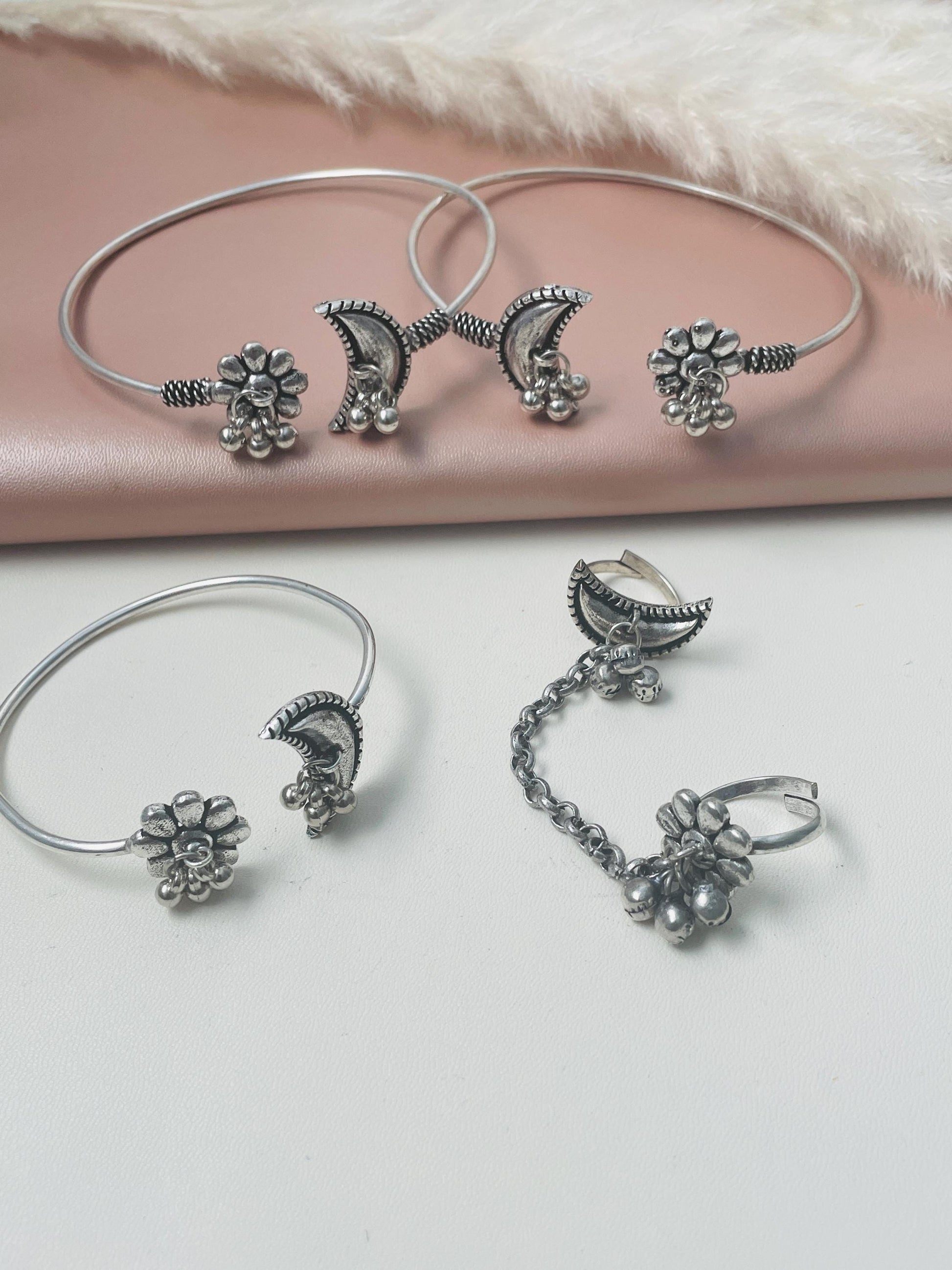 A set of four silver-toned jewelry pieces, including two bracelets and two rings. The bracelets feature a crescent moon design with a floral accent. The rings are also crescent moon shaped with a floral accent and a dangling chain.