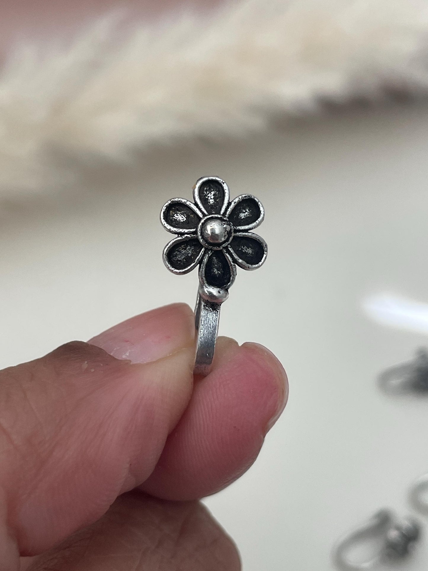 A silver lookalike flower nose ring . The flower has six petals and a round center.