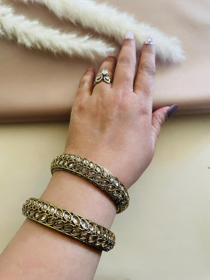 Two gold bangles with clear stones set in a leaf pattern.