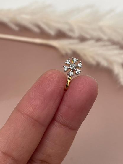 Close-up of a gold nose ring adorned with a cluster of small, clear cubic zirconia stones arranged in a flower-like pattern. The stones are prong-set, and the metal appears to be polished and smooth. The nose ring has a simple, elegant design, suitable for everyday wear or special occasions. The setting is delicate and the stones sparkle.