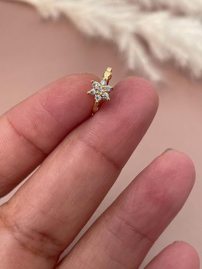Gold flower-shaped nose ring with clear cubic zirconia stones. The nose ring has a delicate, minimalist design, perfect for adding a touch of sparkle to any look.  The floral design features small, sparkling stones set in a gold metal setting. This dainty nose ring is a stylish and subtle accessory.