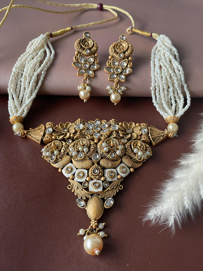 A gold-tone rajwadi finish necklace set with a large, intricate pendant featuring white stones and pearls. The necklace is made of multiple strands of white beads and has a matching pair of earrings with similar designs.