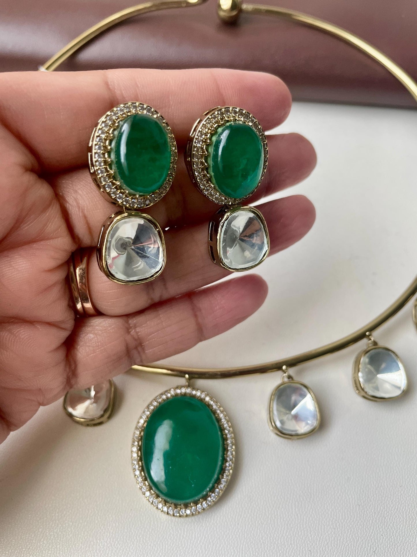A gold choker necklace with a green stone pendant and two matching earrings. The earrings have a green stone with a clear stone underneath. The necklace has four clear stones hanging from it.