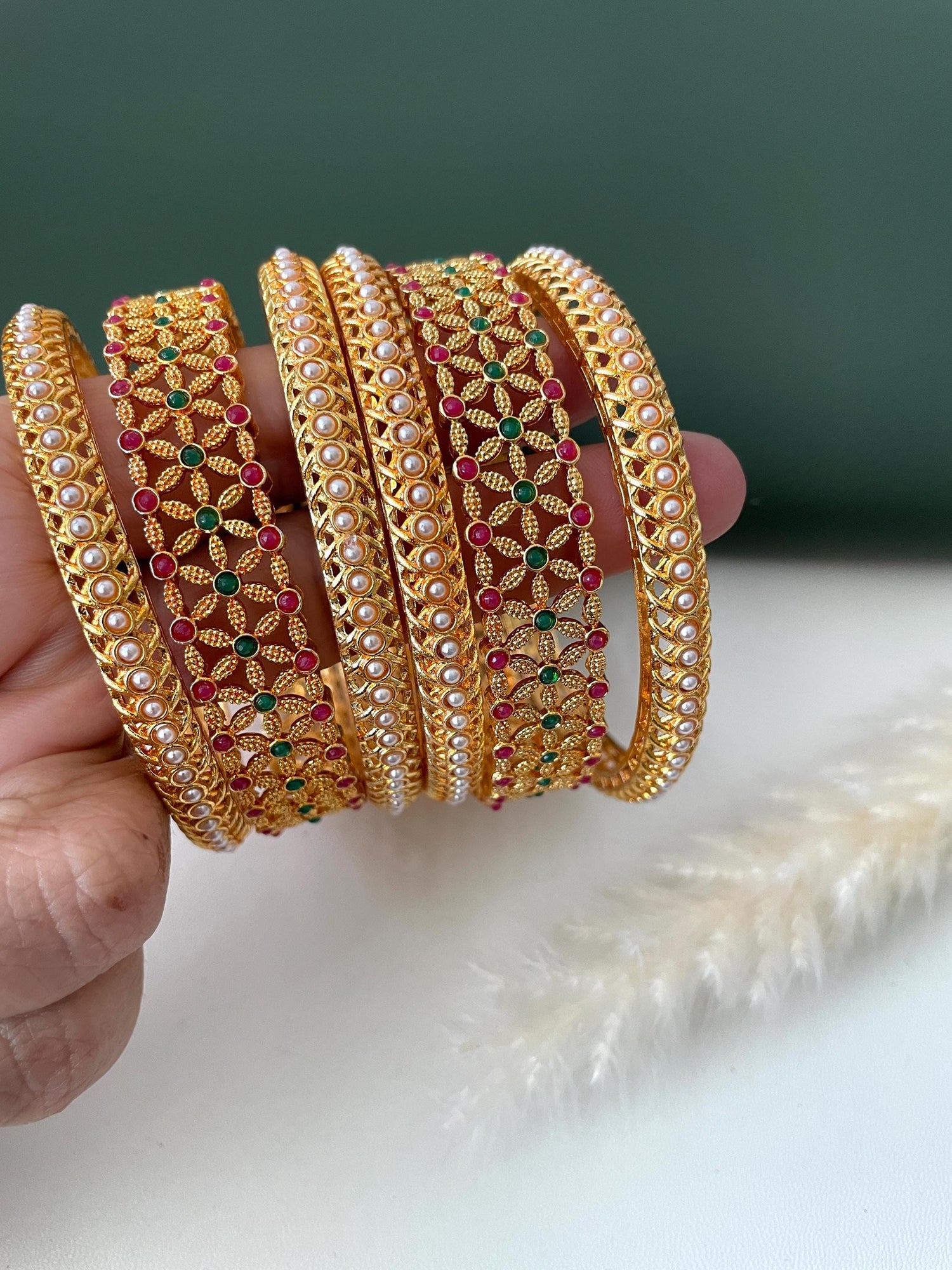 Green and red stone high gold plated bangles with beautiful flower motifs . Comes as set of 6 bangles . 2 flower bangles and 4 pearl bangles