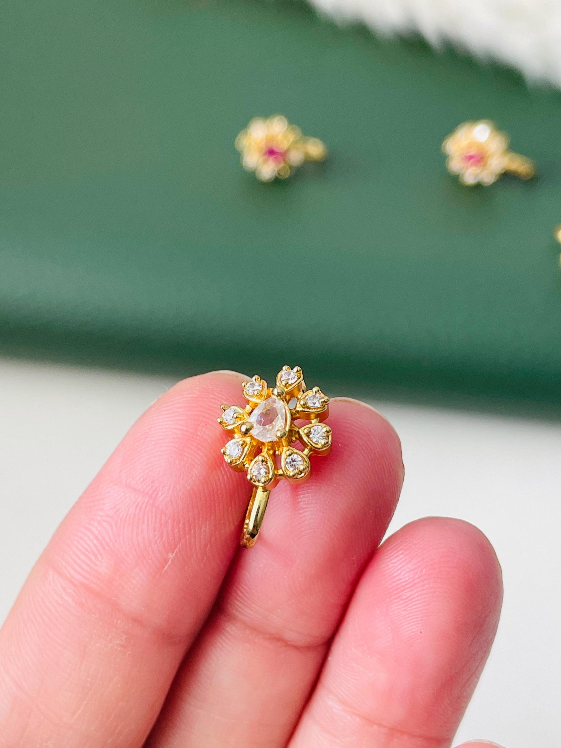 A gold nose ring with a pear-shaped clear stone surrounded by smaller clear stones in a flower shape.