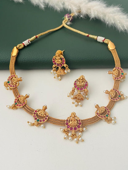 Stunning kemp stone gold plated short necklace set with matching earrings . This simple elegant yet very stunning necklace comes with small jhumkis. Lakshmi and flower motif withRuby and green kemp stones . 16 inches long necklace with adjustable dori .The South Indian temple themed jewelry.