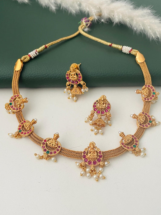 Stunning kemp stone gold plated short necklace set with matching earrings . This simple elegant yet very stunning necklace comes with small jhumkis. Lakshmi and flower motif withRuby and green kemp stones . 16 inches long necklace with adjustable dori .The South Indian temple themed jewelry.