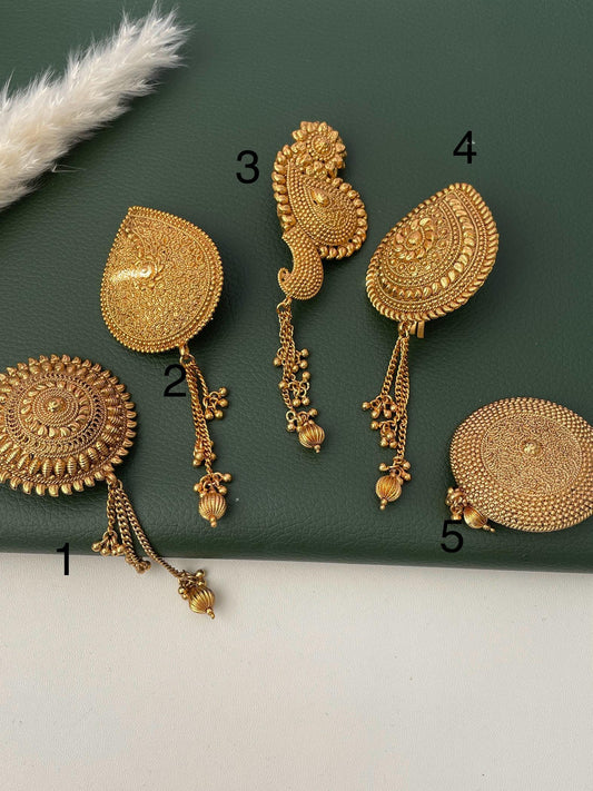 Five gold plated hair clips with intricate designs and dangling chains. The clips are arranged on a green surface.