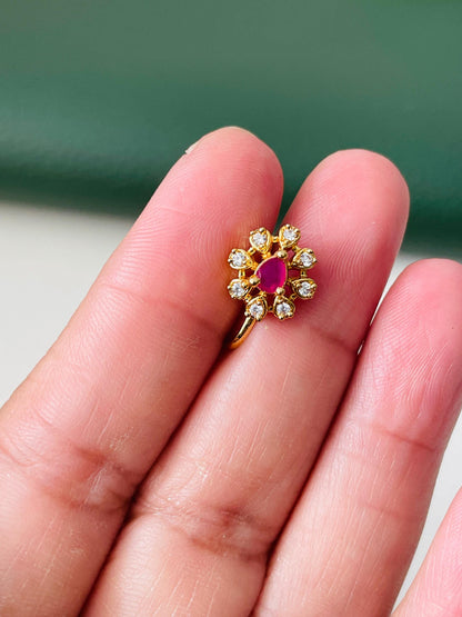 A gold nose ring with a pink stone in the center and a circle of clear stones around it.