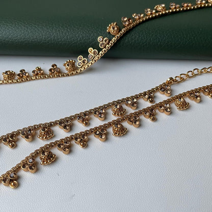 Gold-toned kamarband with floral and gemstone accents. The kambarpatta feature delicate chains and are adorned with small, decorative floral elements and sparkling gemstones. The design is elegant and suitable for various occasions.