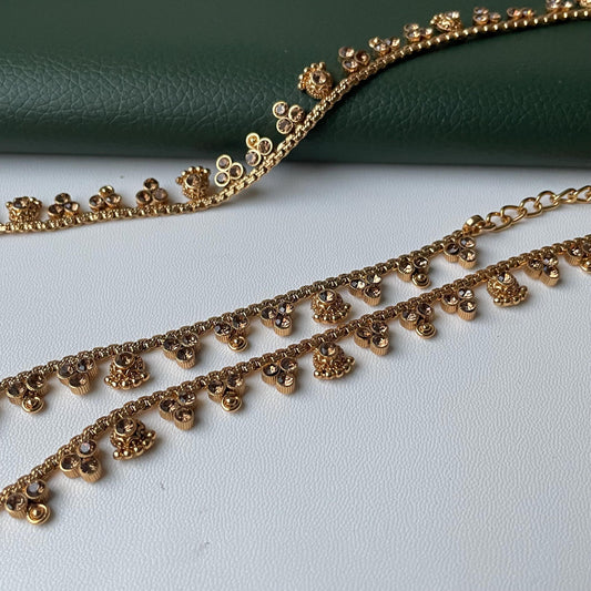 Gold-toned kamarband with floral and gemstone accents. The kambarpatta feature delicate chains and are adorned with small, decorative floral elements and sparkling gemstones. The design is elegant and suitable for various occasions.