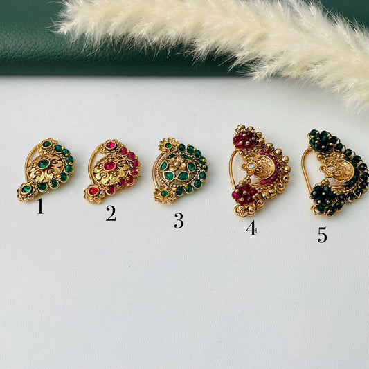 Five ornate gold-toned nose rings with colorful gemstone accents. Designs include green and red stones, with intricate patterns and varying shapes. Each ring is numbered for easy selection.