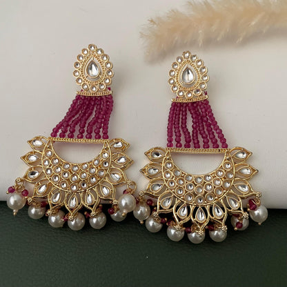 A pair of gold earrings with a teardrop-shaped design, featuring a maroon beaded fringe and white accents.